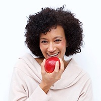 Smiling woman with dental implants in Asheville eating an apple