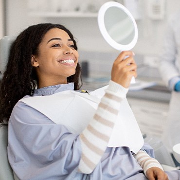 Woman smiling while looking at reflection in handheld mirror