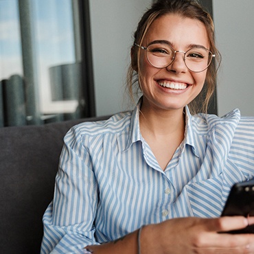 Woman with glasses smiling while holding phone 