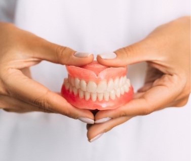 Two hands holding a pair of full dentures