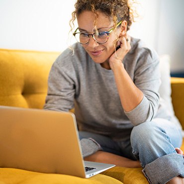 Woman with glasses smiling while looking at laptop