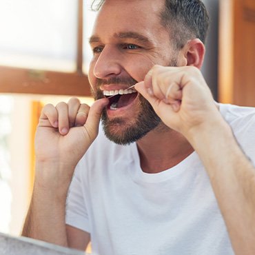 Man smiling while flossing in bathroom