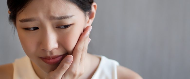 Woman in white shirt rubbing her jaw in pain