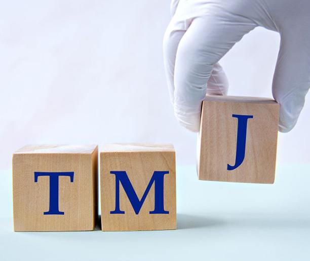 Three wooden blocks that spell out “TMJ”