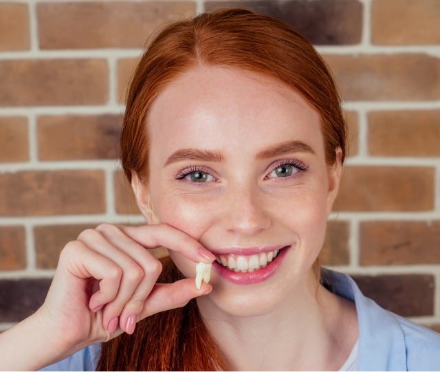 Red haired woman smiling and holding a tooth