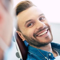 : Man in denim shirt smiling at cosmetic dentist during consultation 