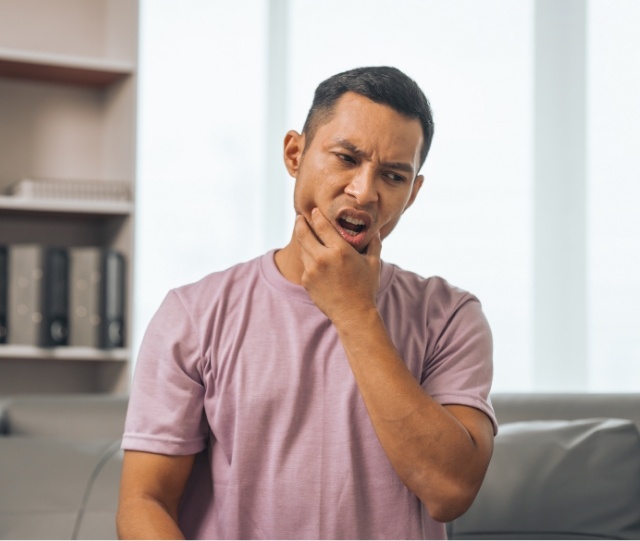 Man in pink shirt rubbing his jaw