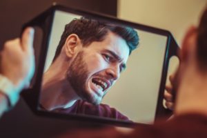 man looking curiously in mirror at teeth