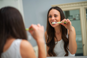 Woman brushing her teeth in a mirror
